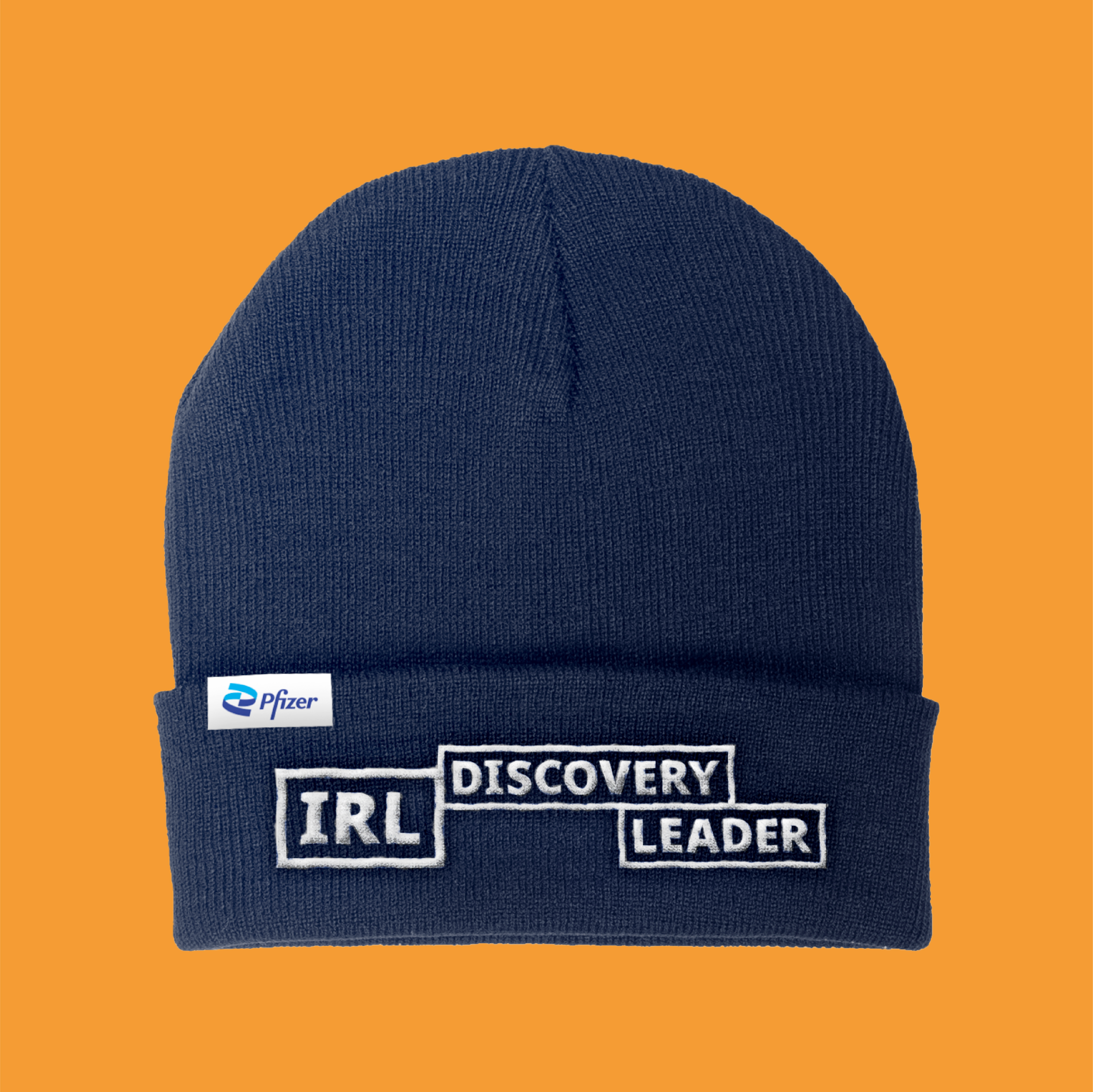 A navy blue knitted beanie with "IRL discovery leader" stitched in white on the cuff and a Pfizer logo sewn on the hem on a bright orange background.