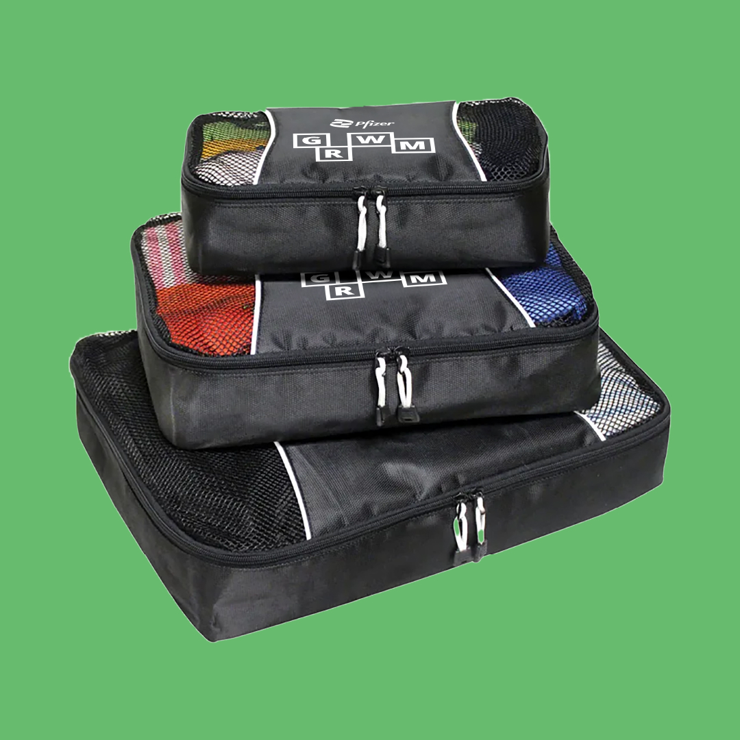 A stack of 3 black packing cubes with “GRWM” printed on top pictured on a green background.