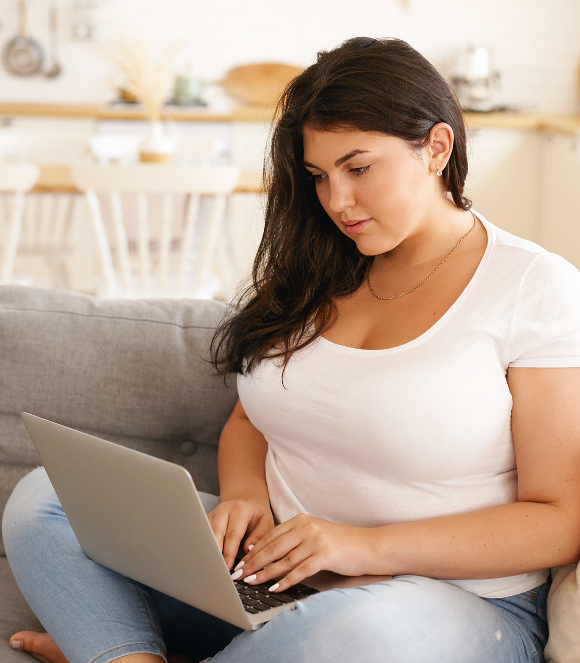A woman sitting on a couch at home using her laptop – Pfizer Clinical Trials