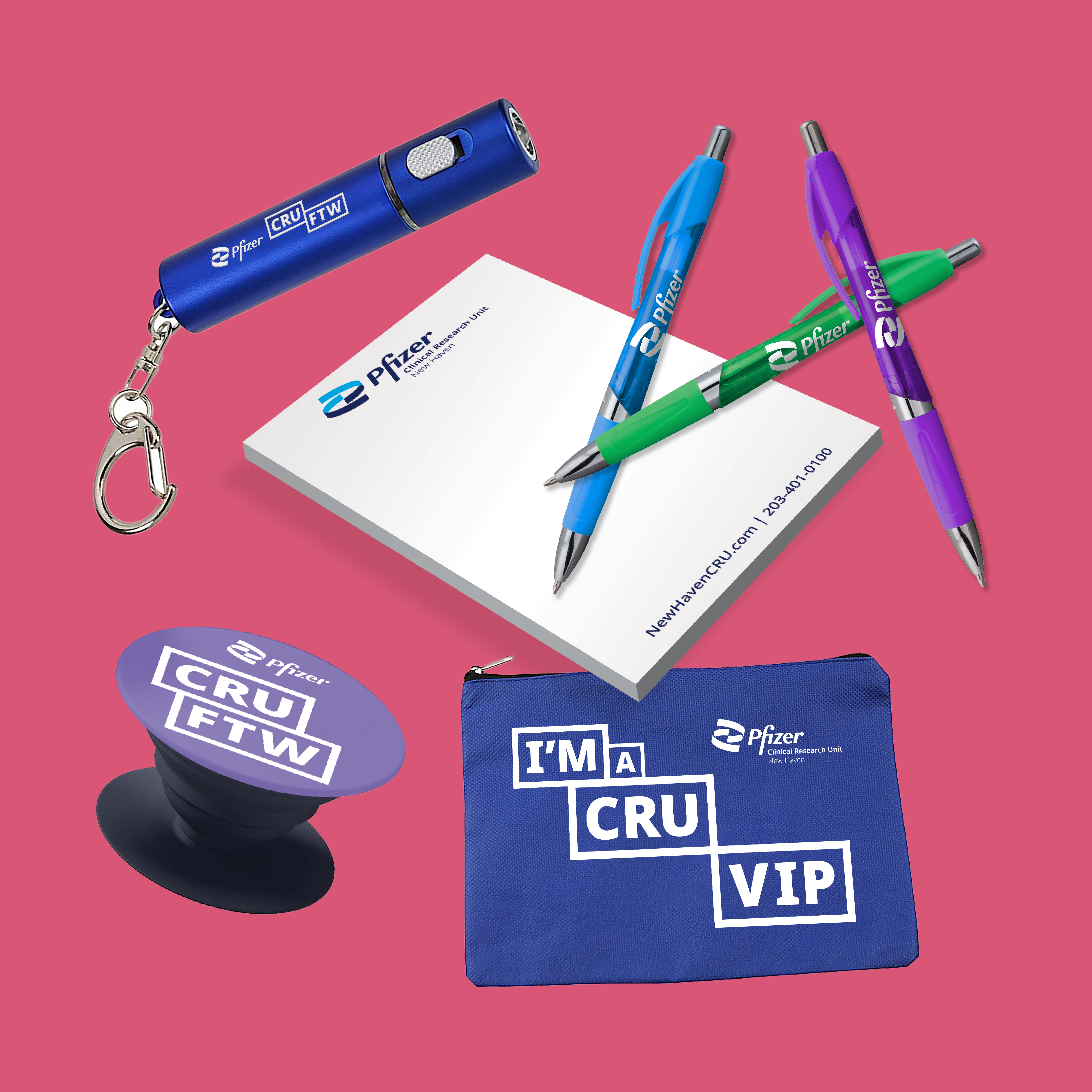 : A collection of colorful promotional PCRU-branded items such as colored pens, note pads, and keychain flashlights on a bright pink background.