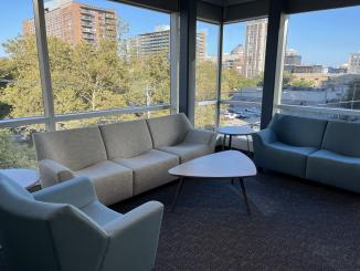 Chairs and sofas along glass windows for vaccine clinical trial participants at the PCRU overlook trees and buildings in downtown New Haven.