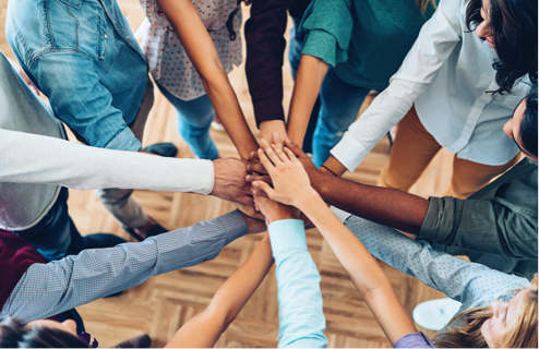 A group of healthy volunteers stack their hands on top of each other while standing in a circle
