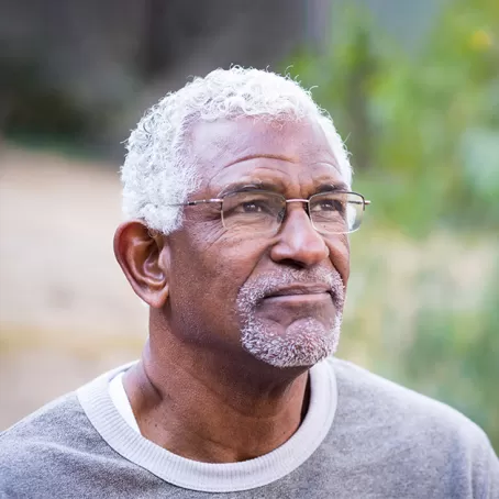 A mature black man with white hair and glasses standing outdoors, looking off into the distance – Pfizer Clinical Trials     