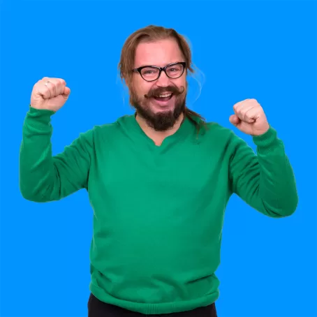 A healthy clinical trial volunteer in a green shirt holds their hands up proudly while smiling against a blue background.