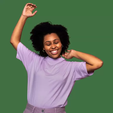 A healthy clinical trial participant in a light purple shirt smiles with their arms held high on a deep green background.