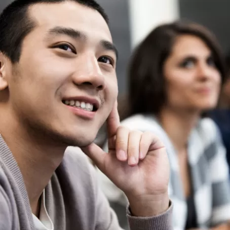 A clinical trial participant smiles at something behind the camera with other people seated in the background.