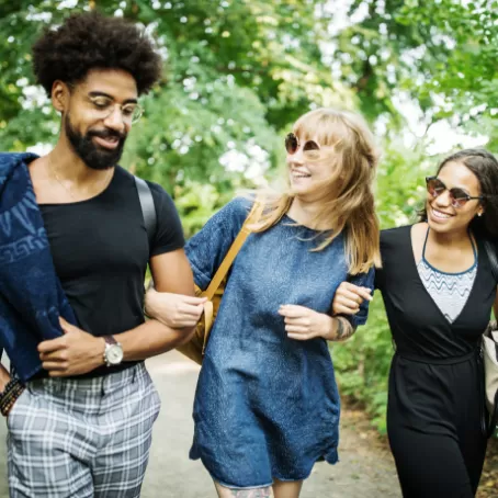 Three young clinical trial participants link elbows while walking outside together.