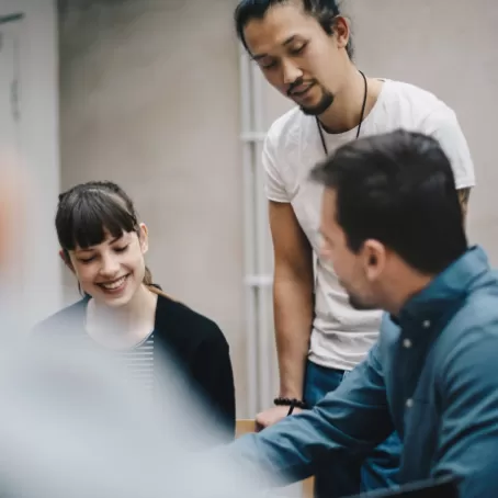 Three young people stand or sit at a table while talking together.