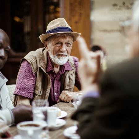 A group of elderly friends, sitting at a table, drinking coffee, and having a conversation – Pfizer Clinical Trials
