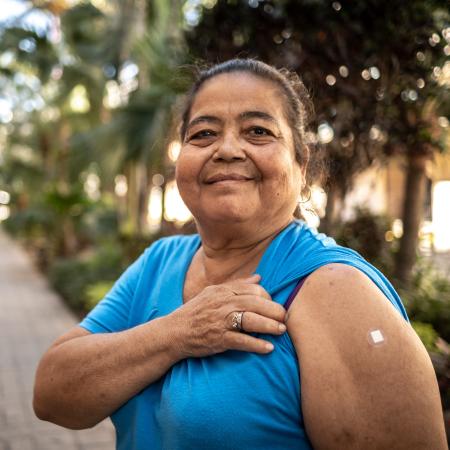 Imagen de una mujer latina al aire libre con una curita en el brazo. – Estudios clínicos de Pfizer