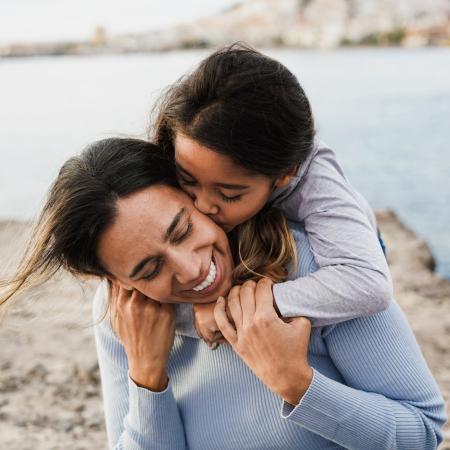 Retrato de una niña abrazando a su madre en la playa –Estudios Clínicos de Pfizer