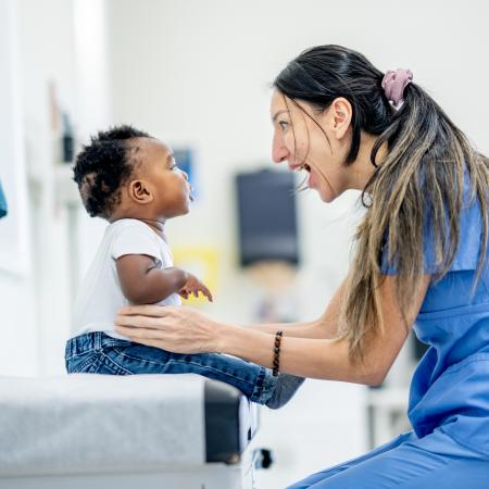 Female healthcare provider smiling at a baby during their clinic visit – Pfizer Clinical Trials