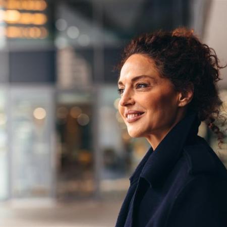 Portrait of a successful businesswoman smiling and looking away, enjoying a moment of quiet contemplation in the bustling environment of a modern building – Pfizer Clinical Trials