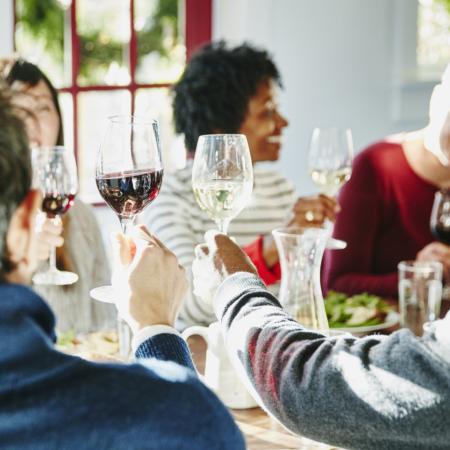A group of people sitting at a dinner table toast their wine glasses