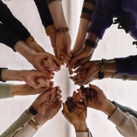 A diverse group of people come together, holding hands in a multi-pointed star pattern with the photo taken from below.